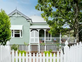 A traditional Queensland cottage with green cladding and white fretwork.