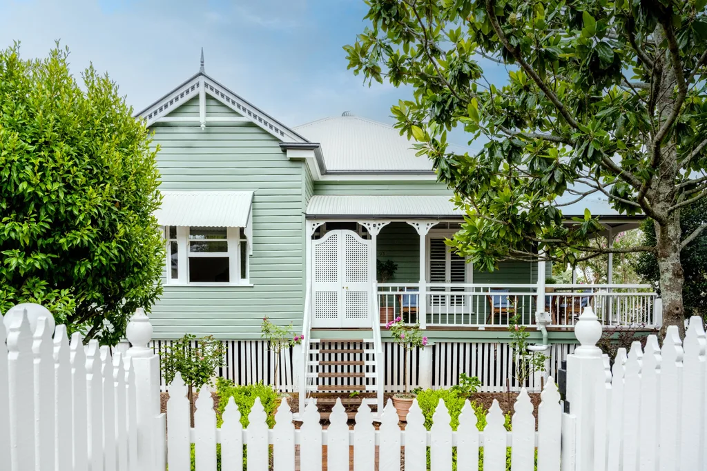 A traditional Queensland cottage with green cladding and white fretwork.