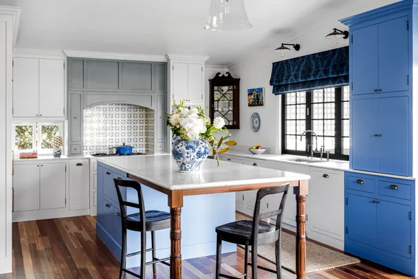 A cottage kitchen with a marble island, blue joinery, a mosaic splashback and farmhouse windows.