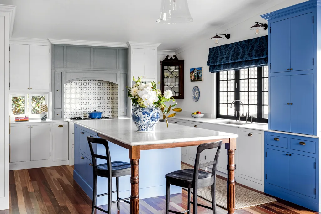 A cottage kitchen with a marble island, blue joinery, a mosaic splashback and farmhouse windows.