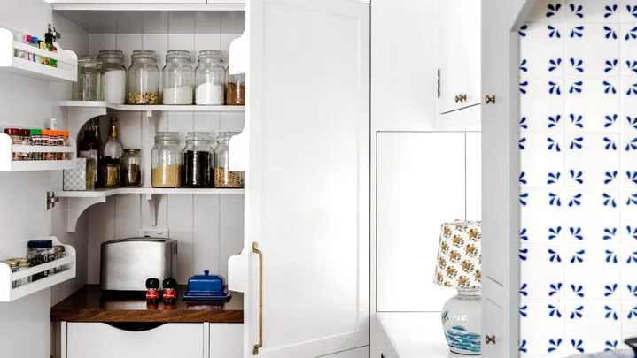 A white open pantry with rattan baskets and shelving.