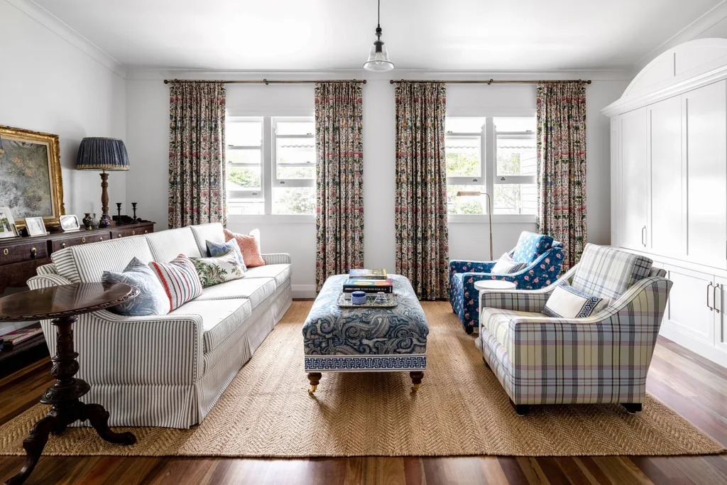 A cottage living room with striped sofa, floral curtains and white cabinets.
