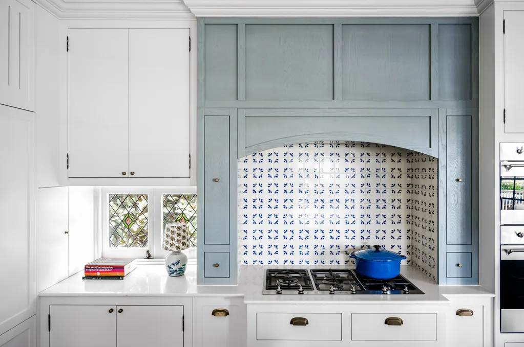 A cottage kitchen with a mosaic splashback, stove top and blue timber joinery.
