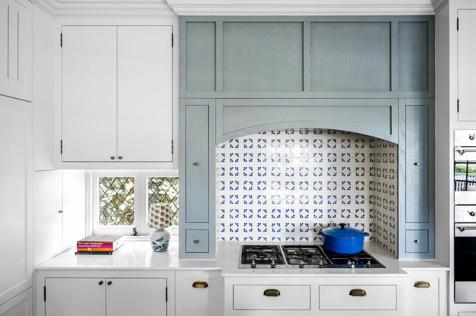 A cottage kitchen with a mosaic splashback, stove top and blue timber joinery.