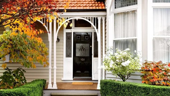 A heritage home exterior with decorative fretwork, leadlight windows and autumn trees.