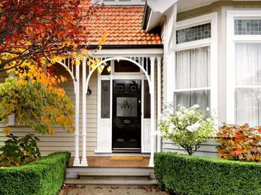 A heritage home exterior with decorative fretwork, leadlight windows and autumn trees.
