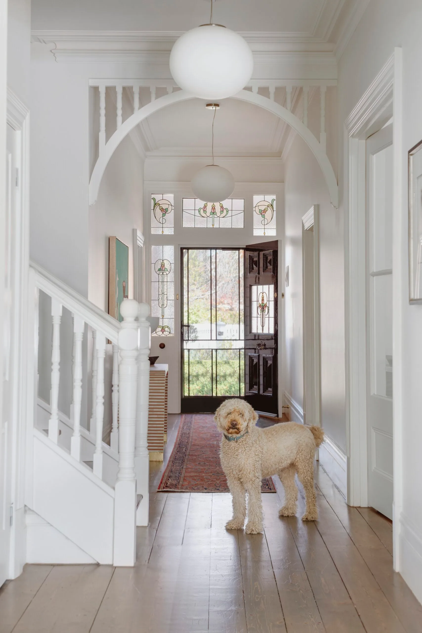 A heritage style hallway with fretwork and a fluffy dog standing by a staircase.