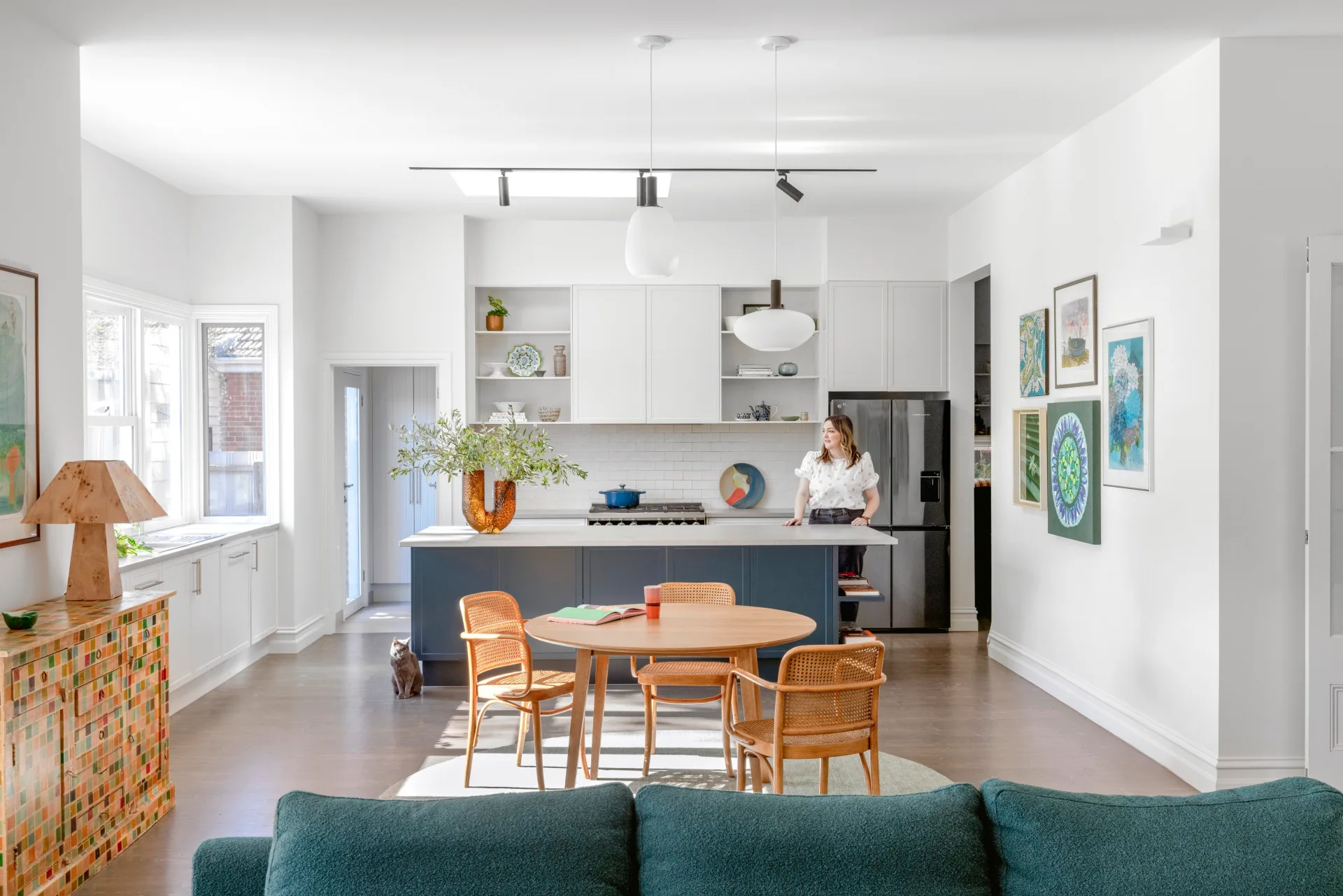 A contemporary kitchen with a blue kitchen island, colourful wall art and a rounded timber table.