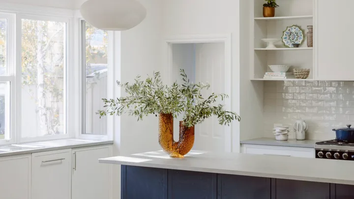 A contemporary kitchen with a blue island, rounded pendants and a timber table.