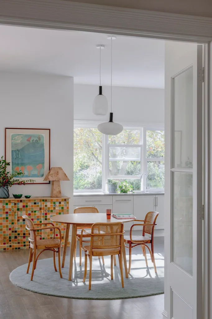 A kitchen eating area with a round table and colourful mosaic sideboard.