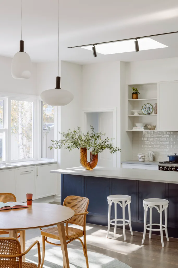 A contemporary kitchen with a blue island, rounded pendants and a timber table.