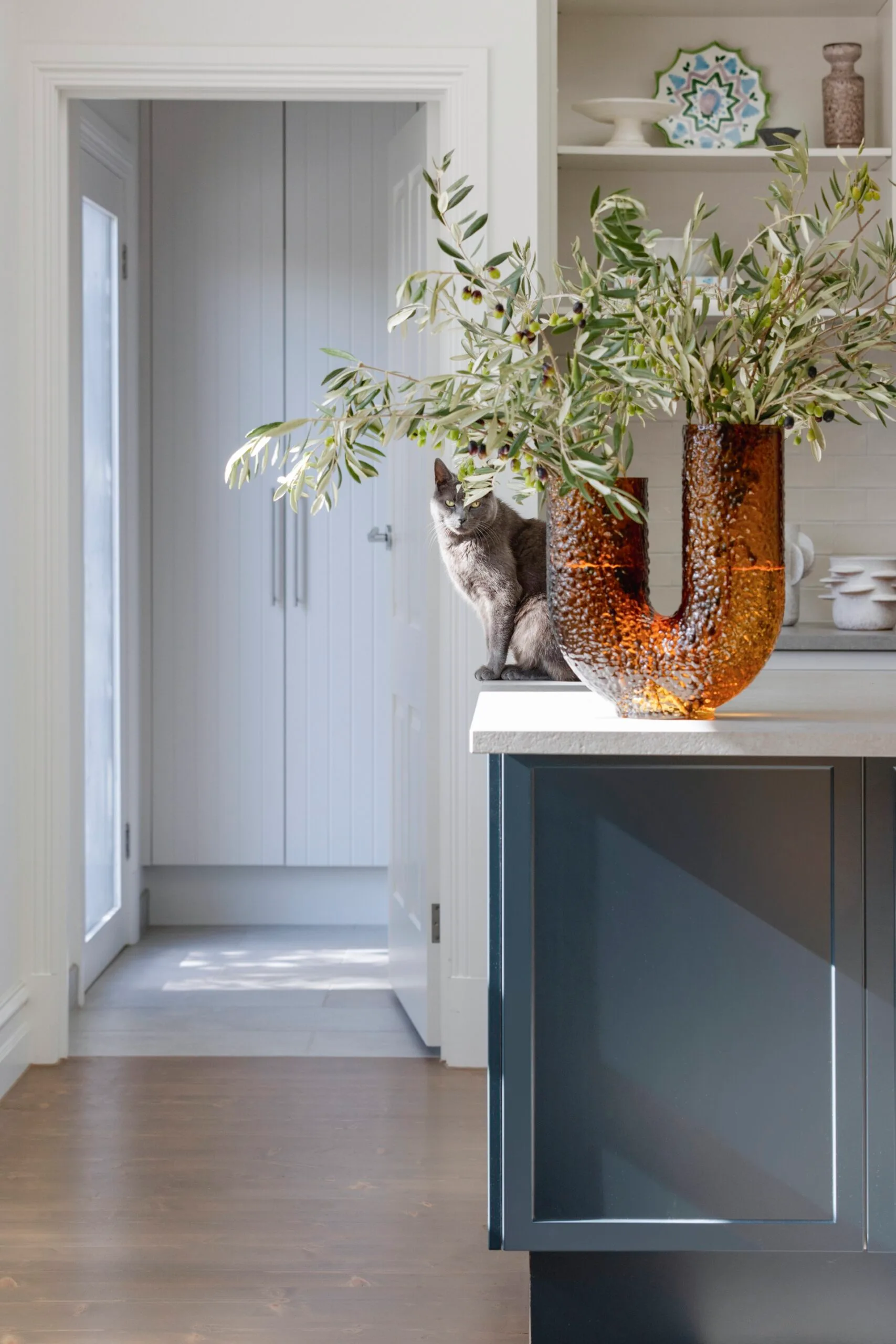 A blue kitchen island with an amber vase and a cat sitting behind it.