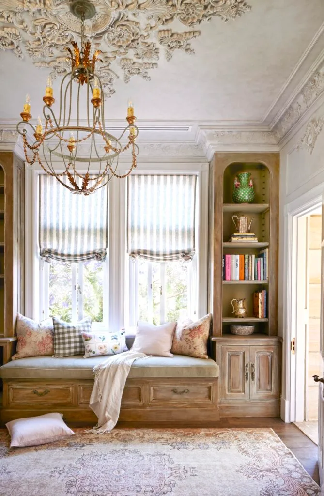 A window seat below a chandelier with decorative ceiling mouldings.