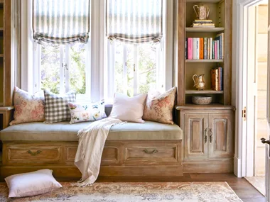 A window seat below a chandelier with decorative ceiling mouldings.