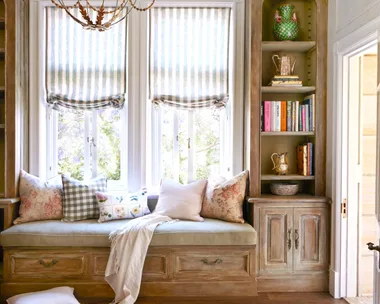 A window seat below a chandelier with decorative ceiling mouldings.