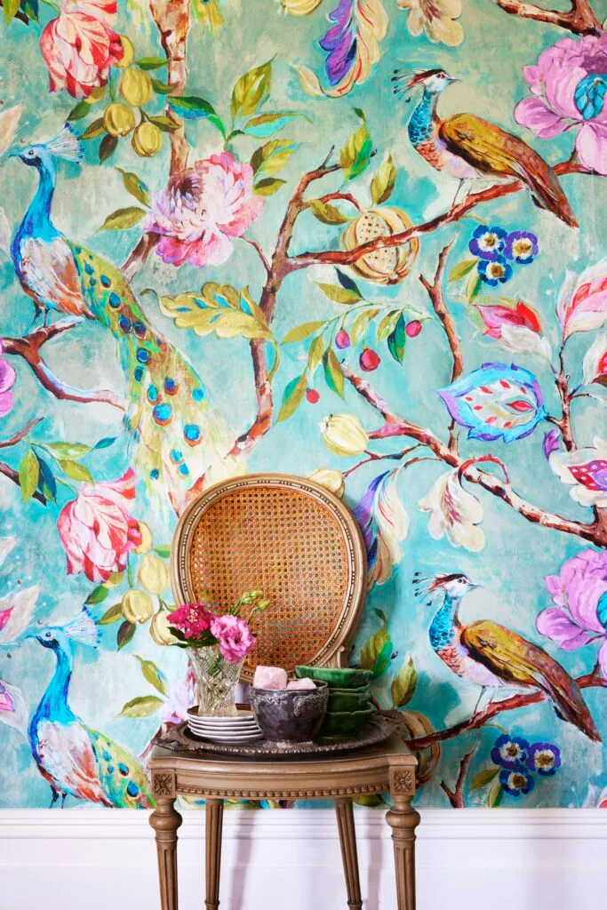 A vintage cane chair beside a wall of decorative peacock wallpaper.