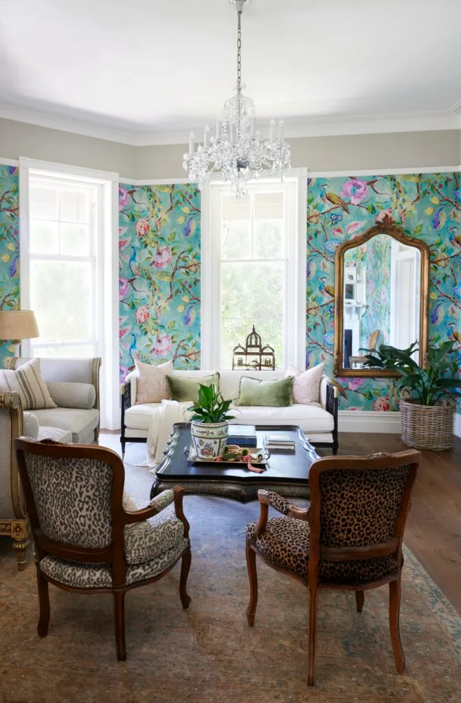 A formal living room with a chandelier, French provincial furniture and blue wallpaper.