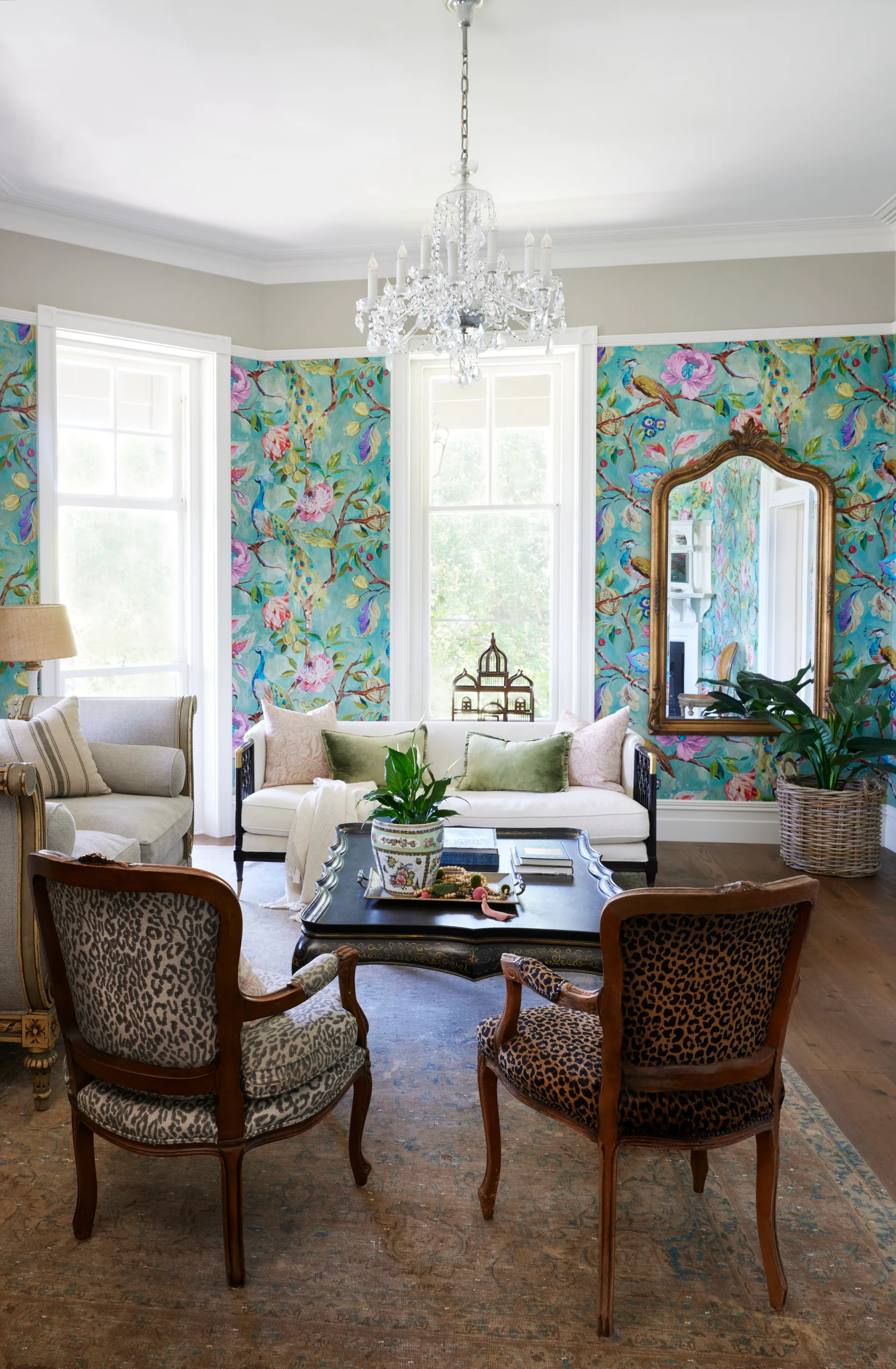 A formal living room with a chandelier, French provincial furniture and blue wallpaper.