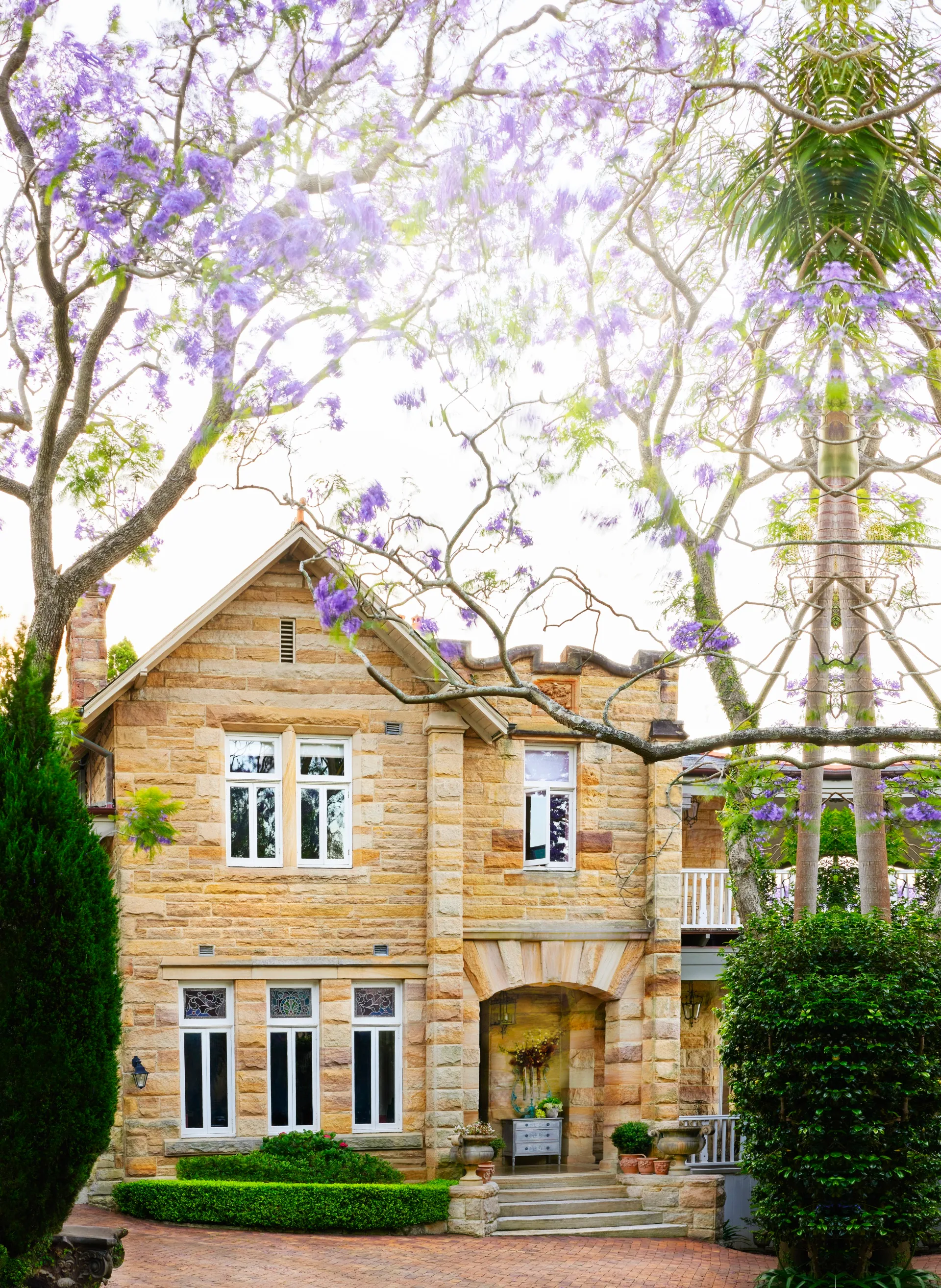 A two-storey sandstone house and jacaranda trees.