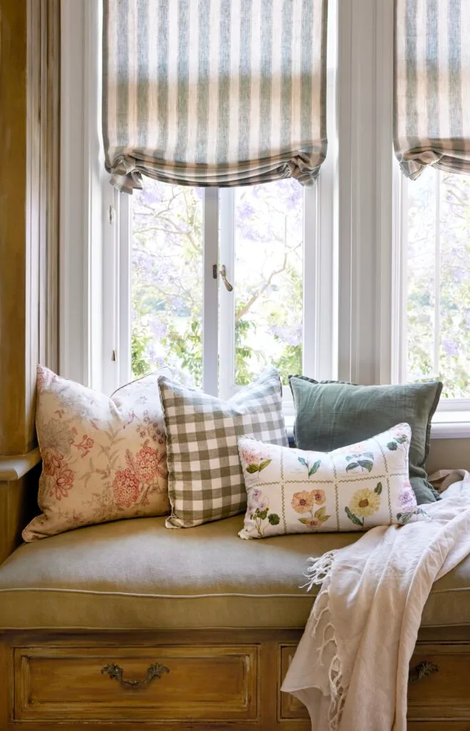 A window seat with cushions and striped curtains.