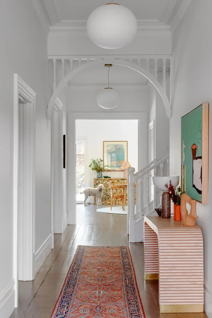 A hallways with red patterned runner, striped sideboard and bright aqua artwork.