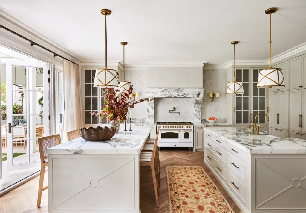 A large classic-style kitchen with two marble islands, a freestanding cooker and hanging lights.