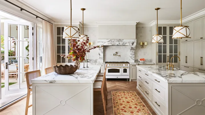 A large classic-style kitchen with two marble islands, a freestanding cooker and hanging lights.