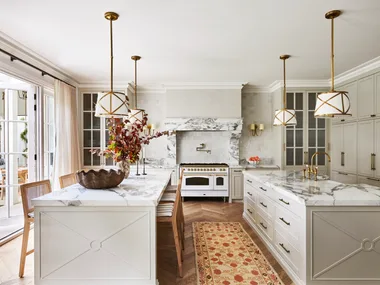 A large classic-style kitchen with two marble islands, a freestanding cooker and hanging lights.