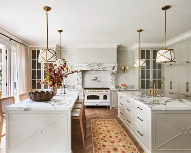 A large classic-style kitchen with two marble islands, a freestanding cooker and hanging lights.