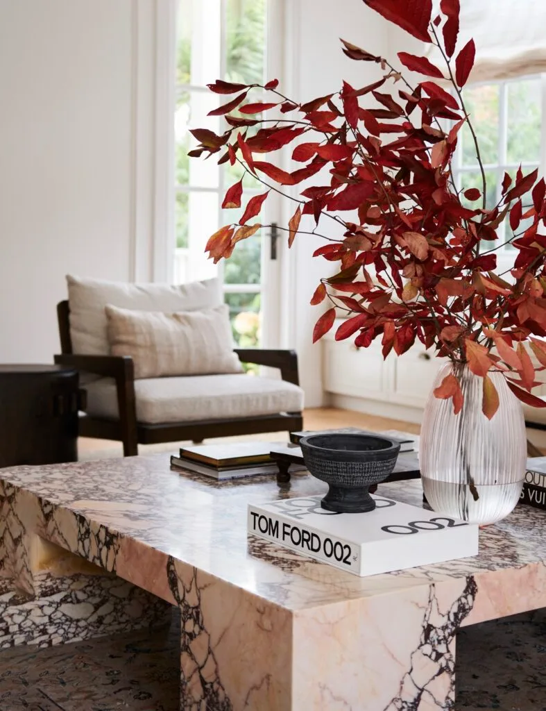 A marble coffee table with a vase of red foliage and a Tom Ford book.