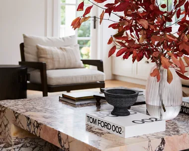 A marble coffee table with a vase of red foliage and a Tom Ford book.
