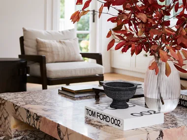 A marble coffee table with a vase of red foliage and a Tom Ford book.