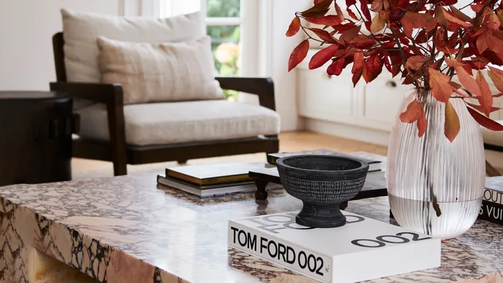 A marble coffee table with a vase of red foliage and a Tom Ford book.