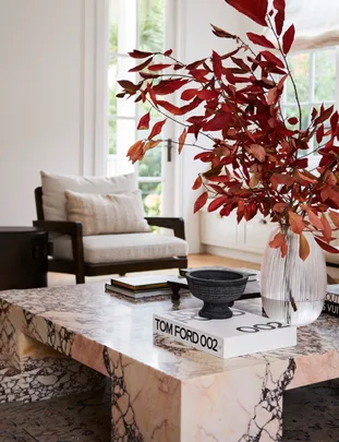 A marble coffee table with a vase of red foliage and a Tom Ford book.