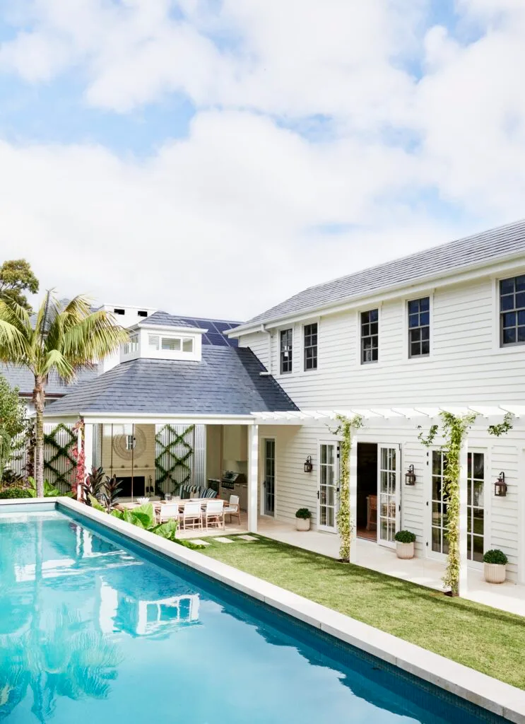 A swimming pool beside the alfresco area with palms and climbing plants.