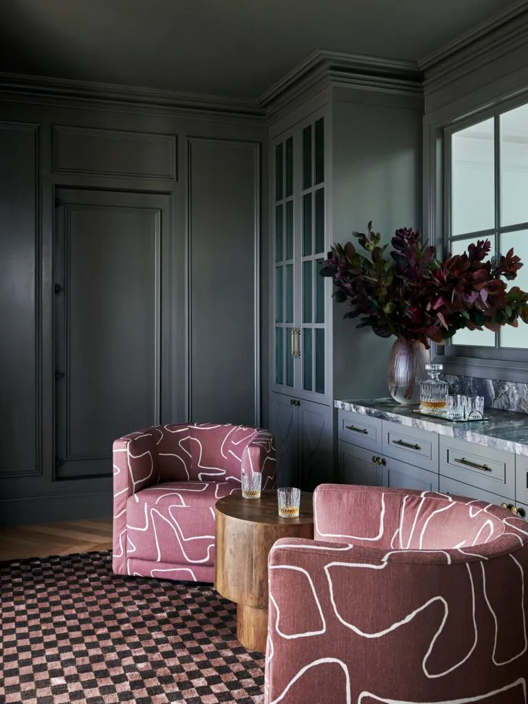 A dark whisky room with mauve armchairs and checked floors.