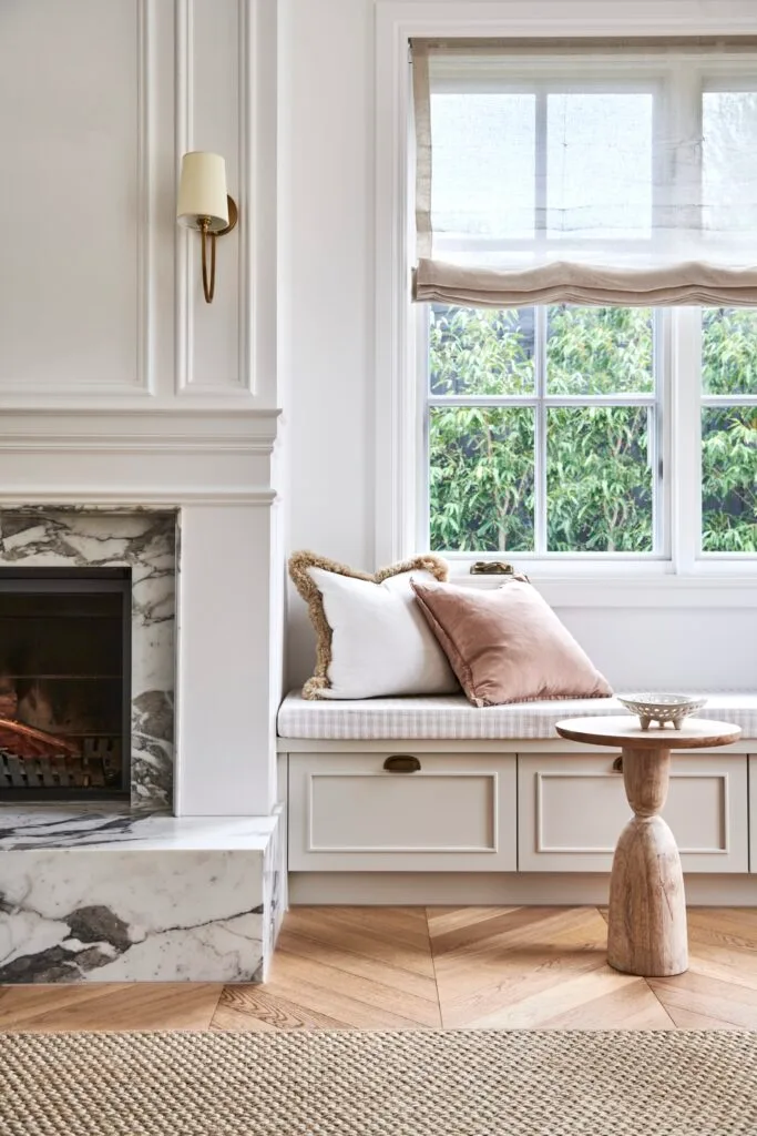 A window seat with shaker drawers beside a marble fireplace.