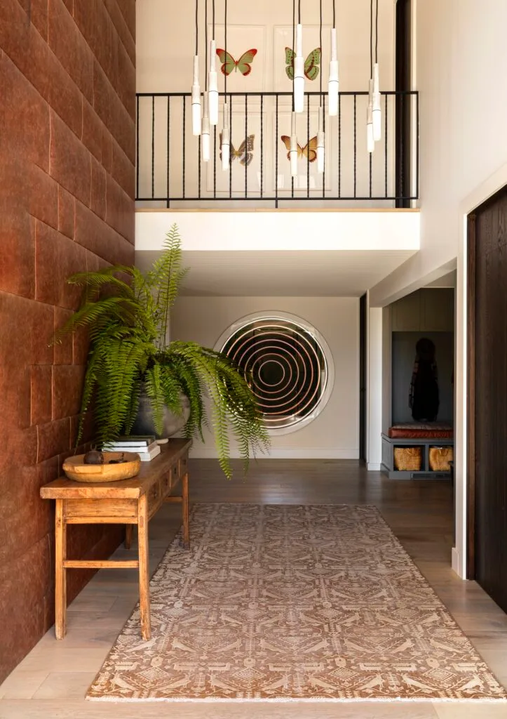 A tall entry way with a leather-clad wall, timber console and circular artwork.