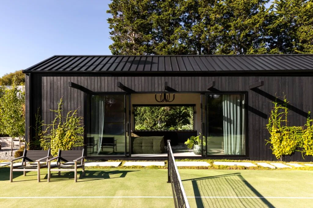 A tennis court beside a black cladded garden pavilion.