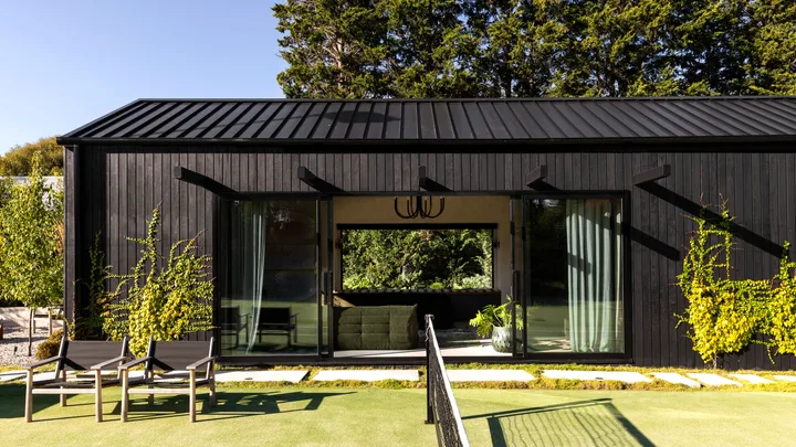A tennis court beside a black cladded garden pavilion.