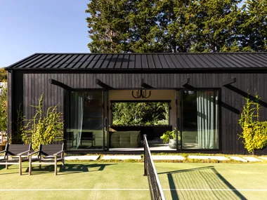 A tennis court beside a black cladded garden pavilion.
