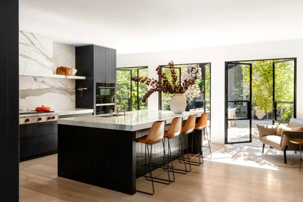 A modern kitchen with a black and marble topped island and open garden doors.