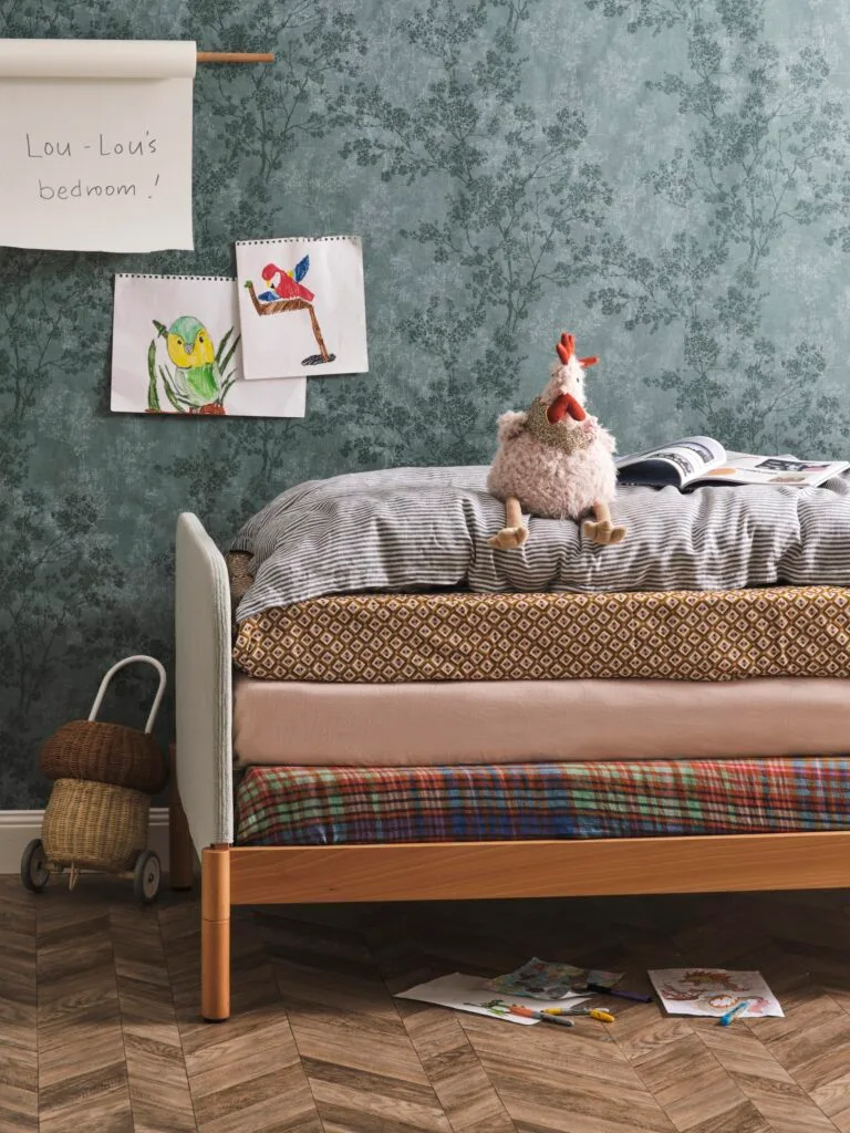 A kid's bedroom with stacked mattresses and green forest wallpaper.