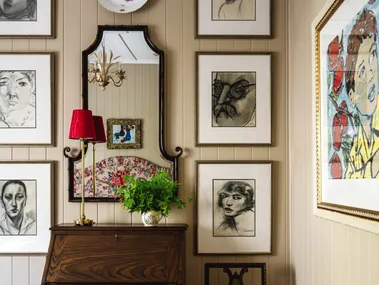 A wall gallery with charcoal drawings over a vintage style cabinet.