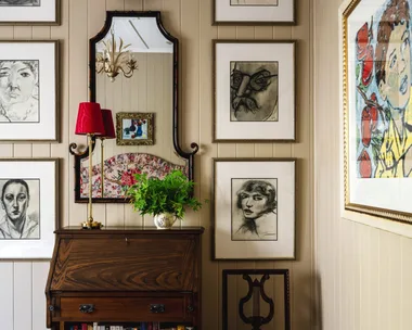 A wall gallery with charcoal drawings over a vintage style cabinet.