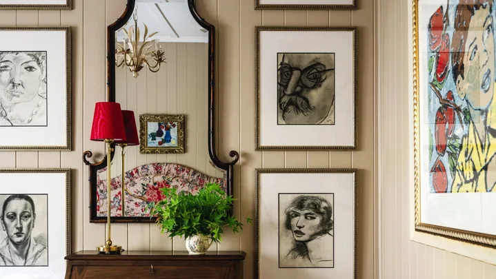 A wall gallery with charcoal drawings over a vintage style cabinet.