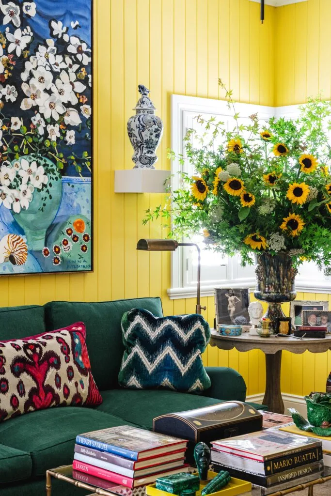 A bright yellow living room with a vase of sunflowers and green sofa.