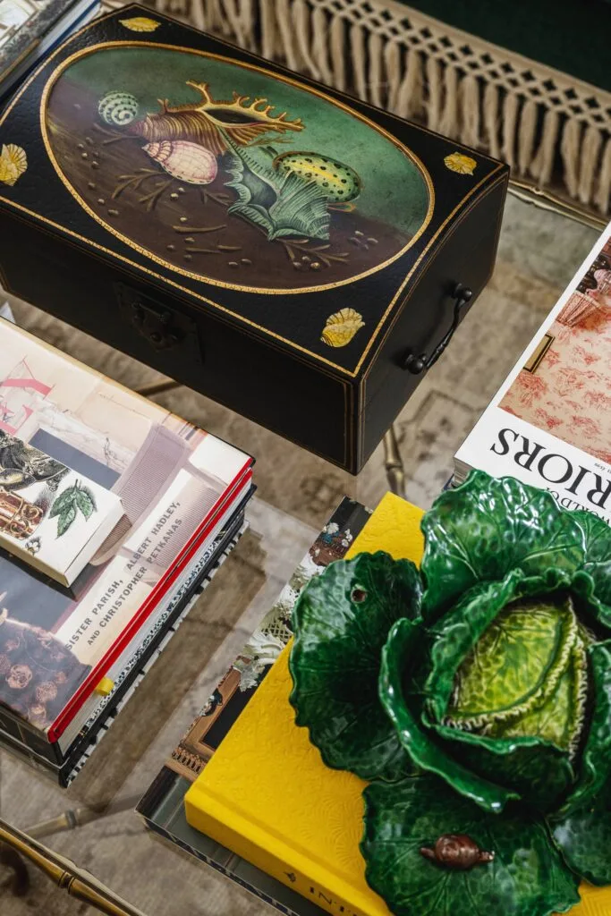 A glass coffee table with books and a painted seashell box.