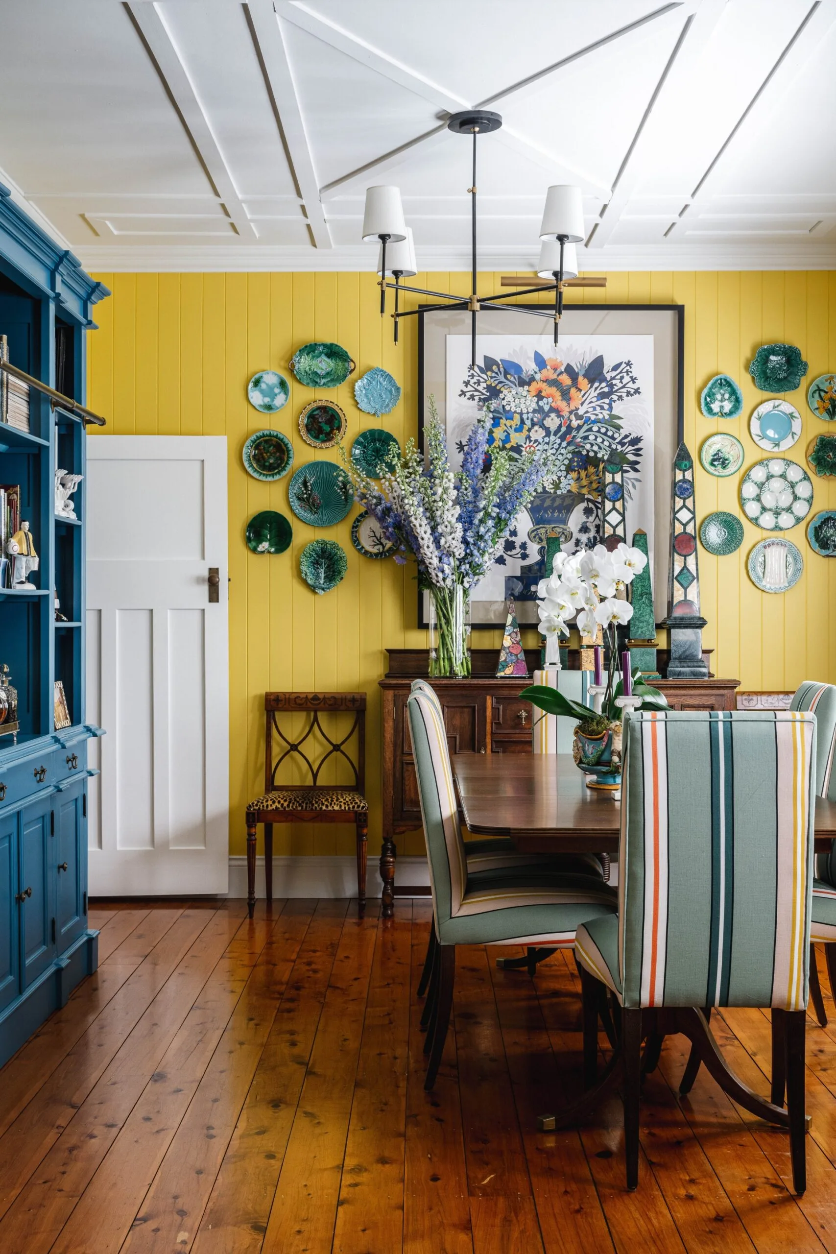 A yellow dining room with a wooden dining table and flooring and a blue cabinet.