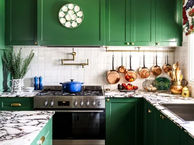 A cottage-style kitchen with green cupboards and a marble island.